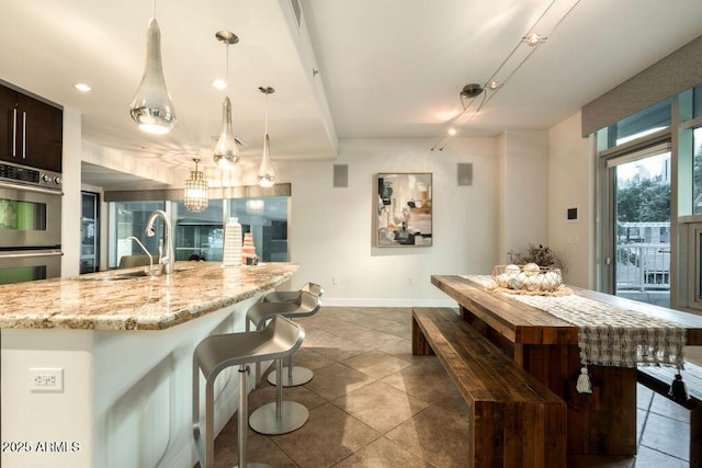 kitchen with sink, light stone counters, decorative light fixtures, dark brown cabinets, and stainless steel double oven