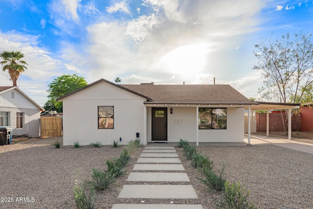 ranch-style home with fence, a shingled roof, an attached carport, and brick siding