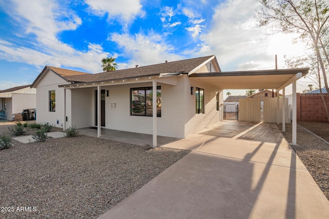 view of front of house featuring a gate, brick siding, fence, concrete driveway, and an attached carport