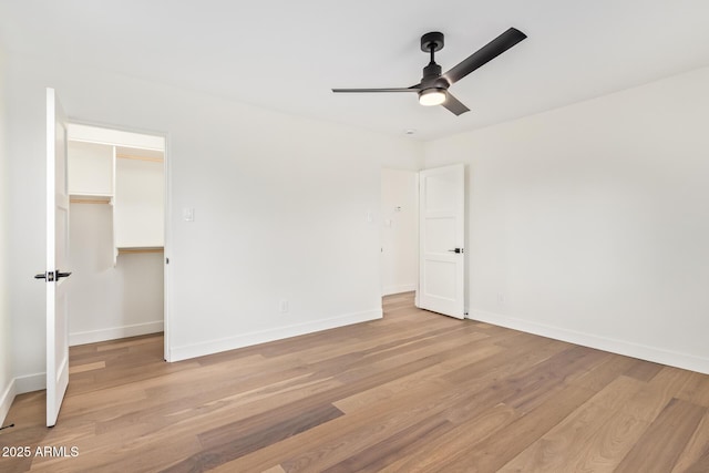 unfurnished bedroom with a ceiling fan, baseboards, a closet, light wood finished floors, and a spacious closet