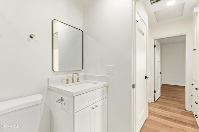 half bath with toilet, baseboards, wood finished floors, and vanity