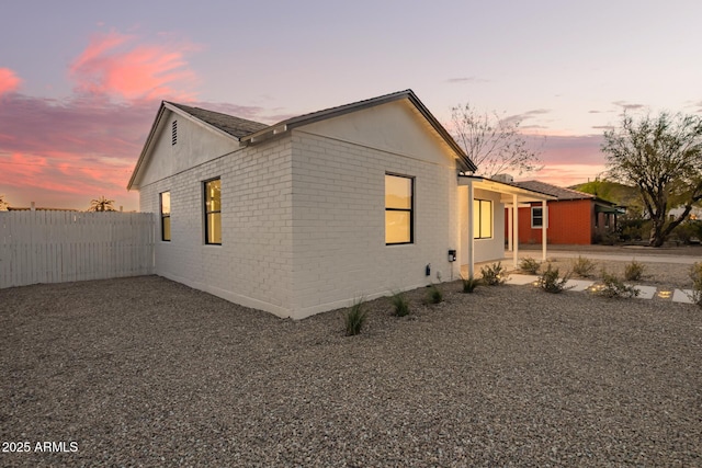 property exterior at dusk with fence and brick siding