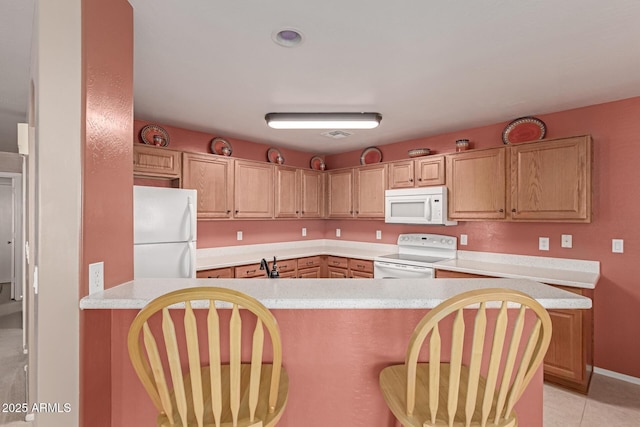 kitchen with white appliances, sink, light tile patterned floors, kitchen peninsula, and a breakfast bar area