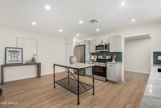 kitchen with appliances with stainless steel finishes, backsplash, light stone counters, and light hardwood / wood-style flooring