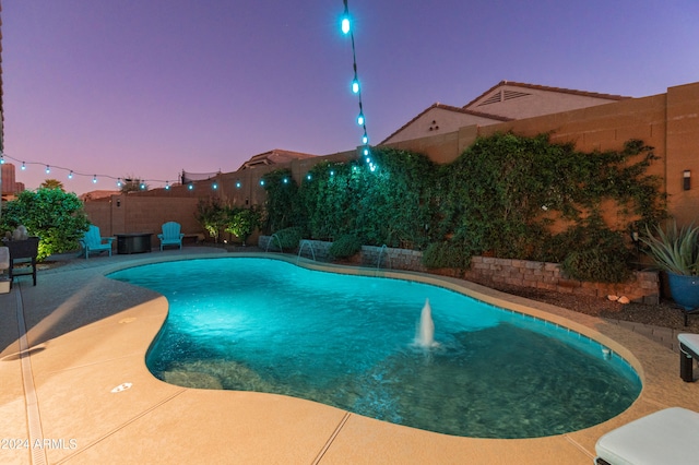 pool at dusk with pool water feature and a patio area