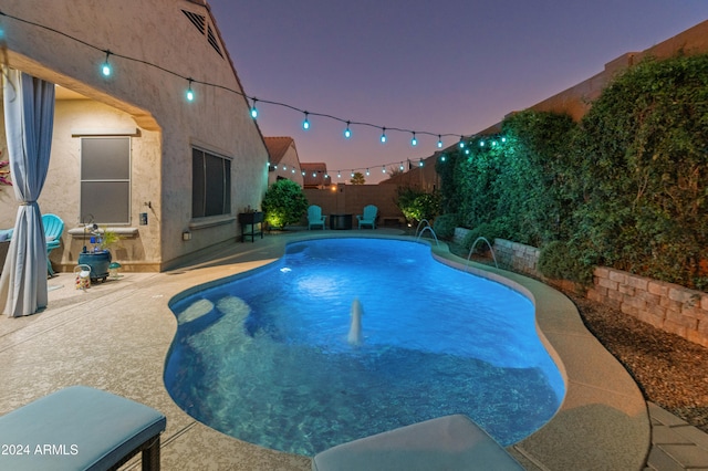 pool at dusk with a patio and pool water feature