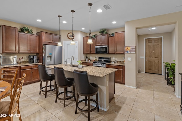 kitchen featuring light stone counters, stainless steel appliances, light tile patterned floors, pendant lighting, and a kitchen island with sink