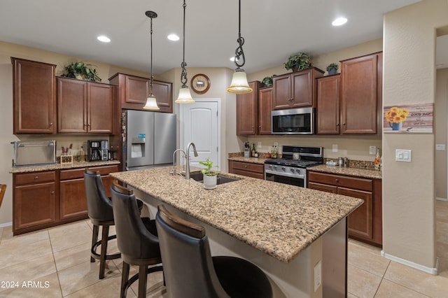 kitchen featuring stainless steel appliances, a center island with sink, hanging light fixtures, sink, and a breakfast bar