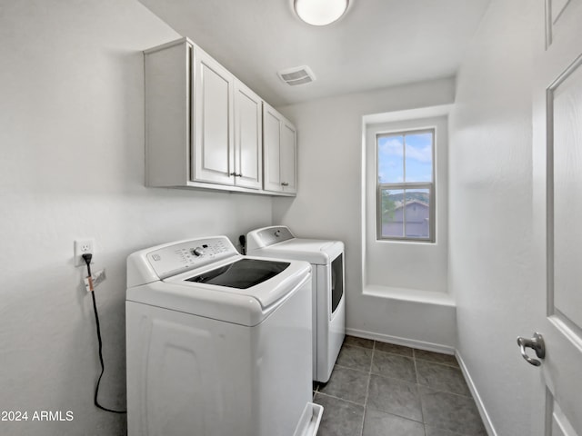 clothes washing area with washer and dryer, dark tile patterned floors, and cabinets