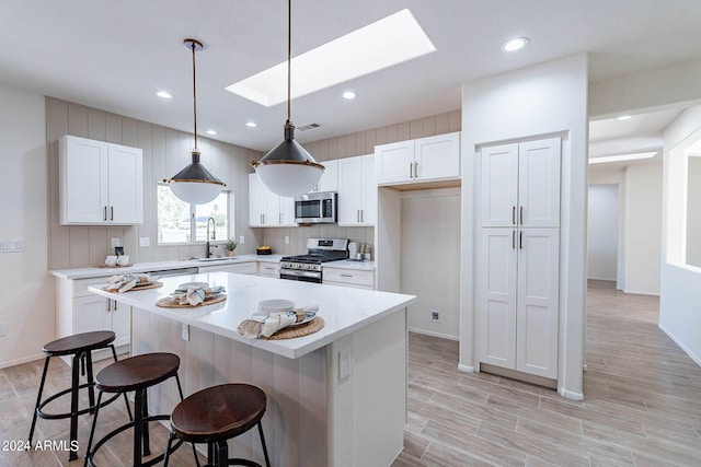 kitchen featuring a skylight, a breakfast bar area, stainless steel appliances, white cabinetry, and a sink