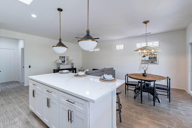 kitchen with white cabinets, pendant lighting, light stone countertops, and a kitchen island