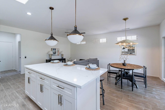 kitchen featuring white cabinets, a breakfast bar, a center island, hanging light fixtures, and wood tiled floor