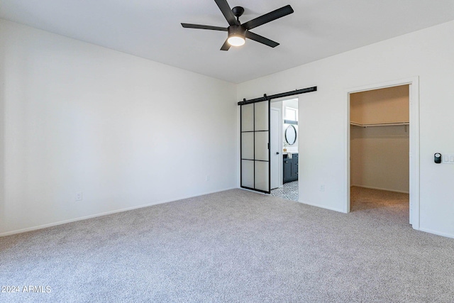 unfurnished bedroom featuring ceiling fan, a walk in closet, light colored carpet, a barn door, and a closet