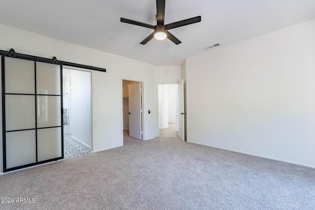 unfurnished bedroom with a barn door, a walk in closet, visible vents, and light colored carpet