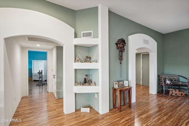 hallway with built in shelves and wood-type flooring