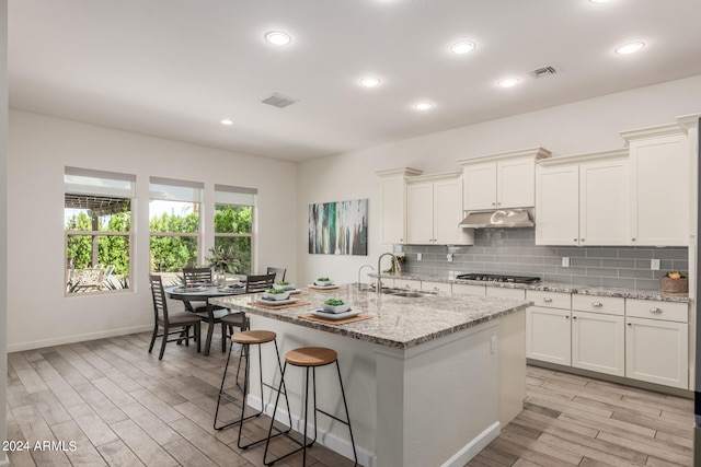 kitchen featuring a kitchen island with sink, a breakfast bar, sink, light wood-type flooring, and white cabinets