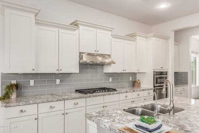 kitchen featuring backsplash, sink, light stone countertops, and appliances with stainless steel finishes