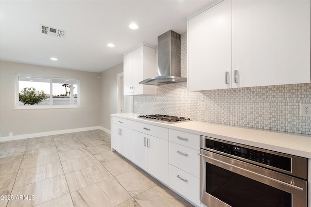 kitchen featuring light tile patterned floors, appliances with stainless steel finishes, decorative backsplash, wall chimney exhaust hood, and white cabinets