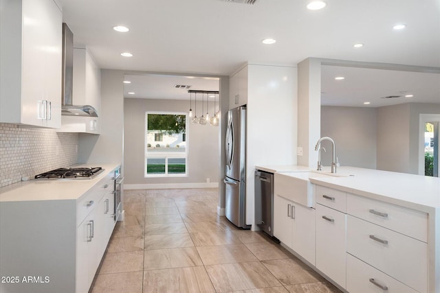 kitchen featuring white cabinets, appliances with stainless steel finishes, wall chimney range hood, and pendant lighting