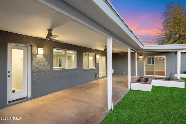 exterior entry at dusk featuring ceiling fan, a patio area, and a lawn