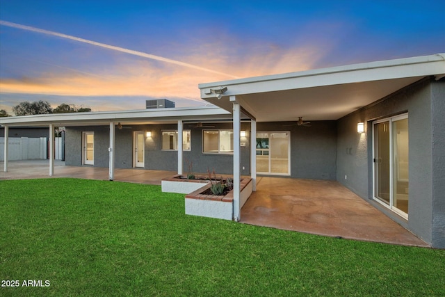 back house at dusk with ceiling fan, a lawn, and a patio