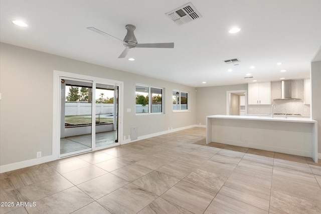 kitchen featuring white cabinetry, ceiling fan, decorative backsplash, wall chimney range hood, and sink