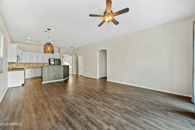 unfurnished living room featuring baseboards, ceiling fan, arched walkways, and dark wood-style flooring