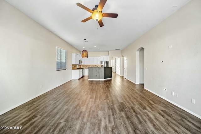 unfurnished living room with dark wood-style floors, arched walkways, recessed lighting, a ceiling fan, and baseboards