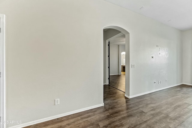 spare room featuring dark wood-style floors, arched walkways, and baseboards