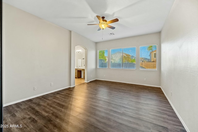 empty room with arched walkways, ceiling fan, visible vents, baseboards, and dark wood finished floors