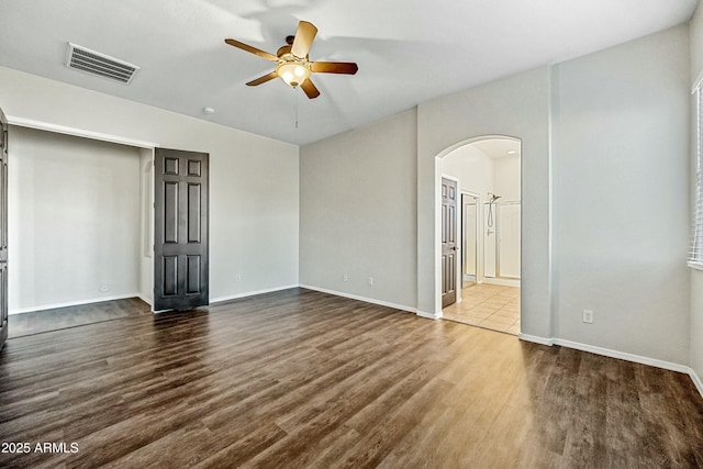 unfurnished bedroom with baseboards, visible vents, arched walkways, ceiling fan, and wood finished floors