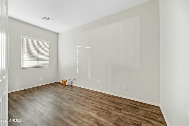 empty room featuring dark wood-type flooring, visible vents, and baseboards