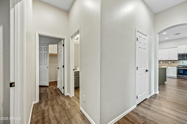 corridor with baseboards, visible vents, arched walkways, and dark wood finished floors