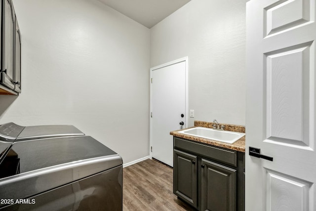 laundry area featuring washing machine and dryer, wood finished floors, a sink, baseboards, and cabinet space