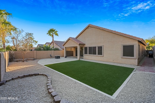 rear view of house featuring a fenced backyard, a tile roof, a lawn, stucco siding, and a patio area