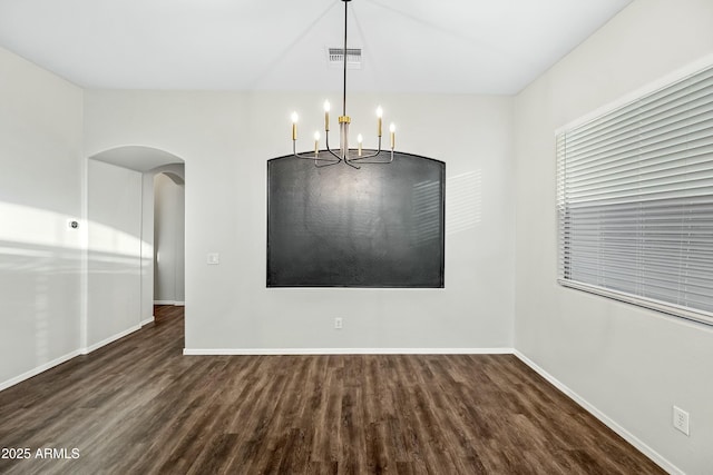 empty room with arched walkways, visible vents, baseboards, and wood finished floors