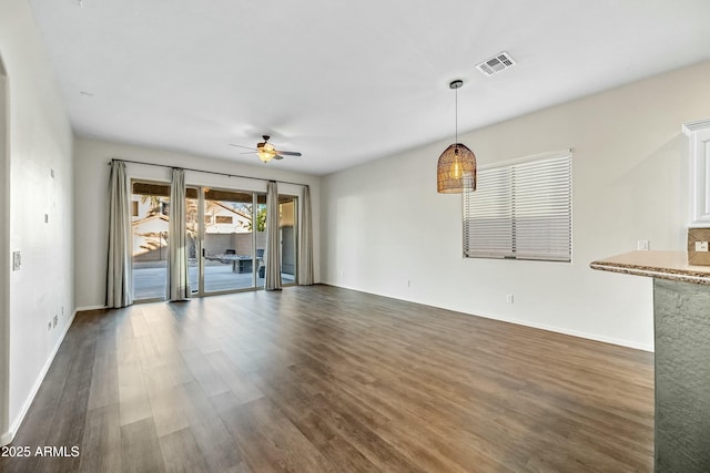 unfurnished living room featuring dark wood-type flooring, visible vents, ceiling fan, and baseboards