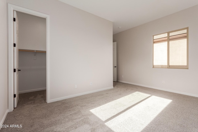 unfurnished bedroom featuring carpet flooring, a walk in closet, and a closet