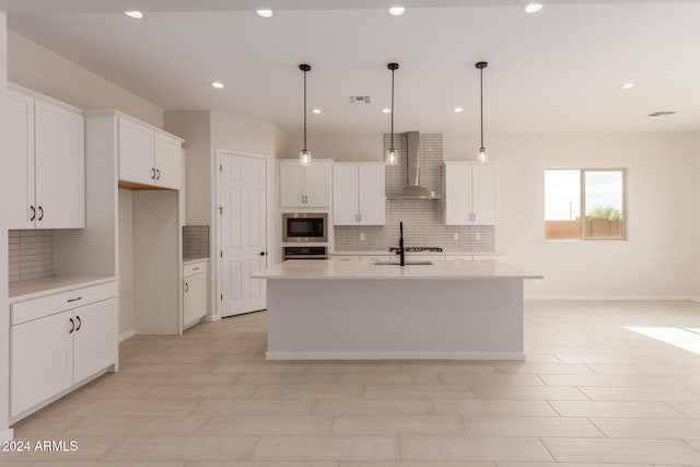 kitchen with built in microwave, a kitchen island with sink, wall chimney range hood, white cabinetry, and hanging light fixtures