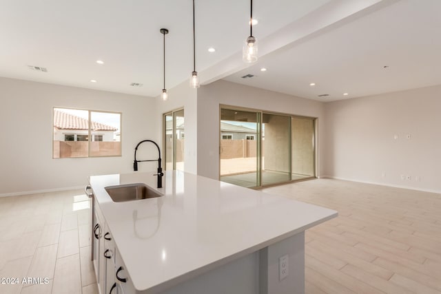 kitchen featuring sink, a center island with sink, light hardwood / wood-style flooring, white cabinets, and hanging light fixtures