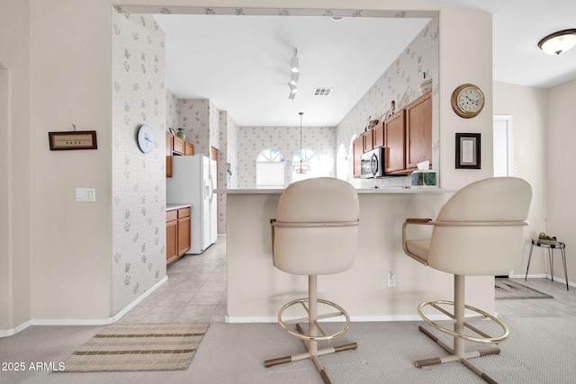 kitchen featuring a breakfast bar area, track lighting, kitchen peninsula, white fridge with ice dispenser, and pendant lighting