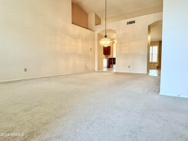 unfurnished living room with an inviting chandelier, carpet, and high vaulted ceiling