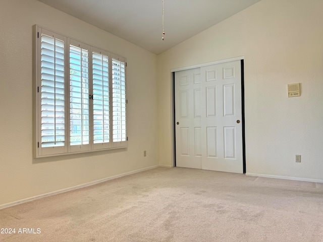 unfurnished bedroom with lofted ceiling, a closet, and light colored carpet