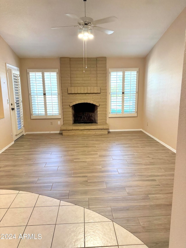 unfurnished living room with a brick fireplace, light hardwood / wood-style floors, plenty of natural light, and ceiling fan