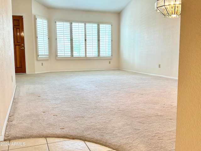 unfurnished room featuring light carpet and an inviting chandelier