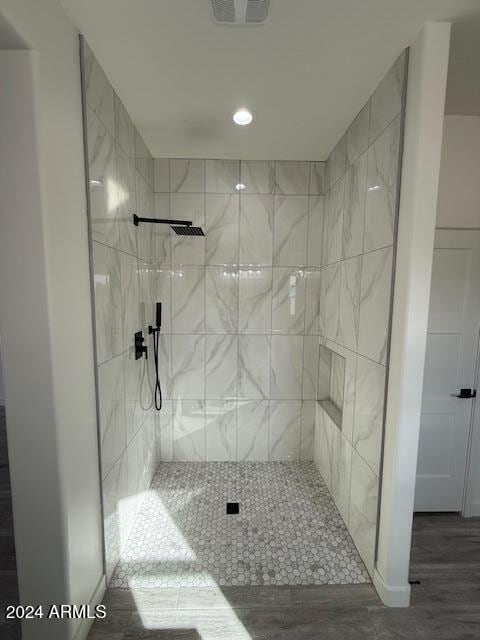 full bathroom with visible vents, wood finished floors, and a tile shower