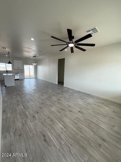 unfurnished living room featuring ceiling fan with notable chandelier, wood finished floors, visible vents, and baseboards