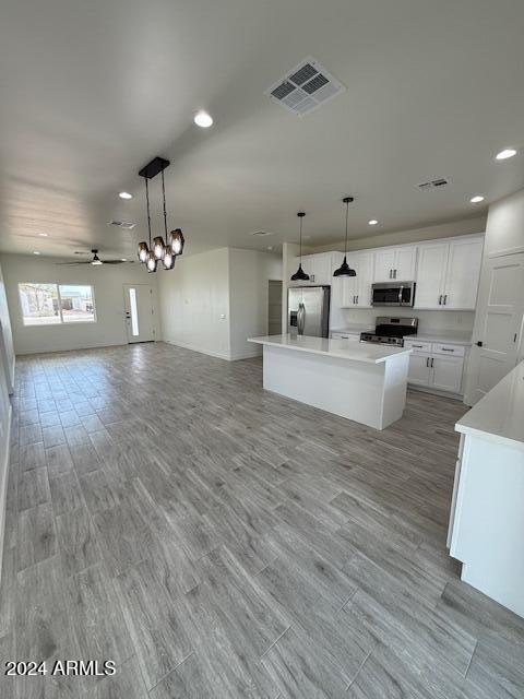 kitchen featuring appliances with stainless steel finishes, ceiling fan with notable chandelier, a kitchen island, white cabinetry, and hanging light fixtures