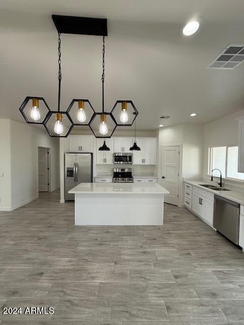 kitchen with visible vents, a sink, a kitchen island, appliances with stainless steel finishes, and light countertops