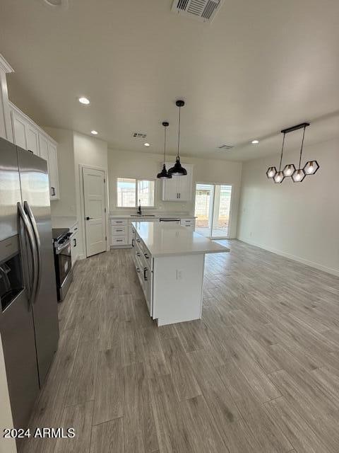 kitchen featuring white cabinetry, stainless steel appliances, pendant lighting, a kitchen island, and light wood-type flooring